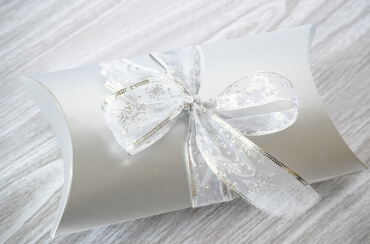 Silver pillow box wrapped with white and silver ribbon with cinnamon glazed pecan inside